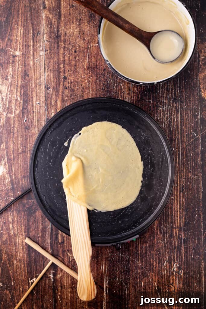 Partially cooked eggnog crepe being gently lifted with a wooden spatula from the pan, indicating readiness for flipping.