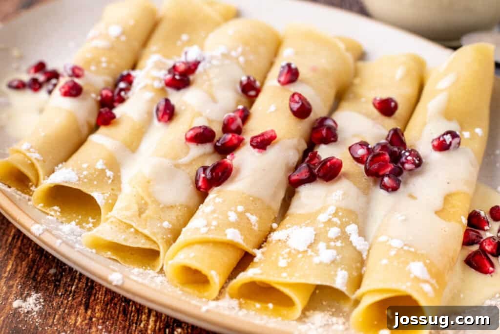 Angled view of golden eggnog crepes topped with creamy eggnog sauce and fresh pomegranate arils on a rustic serving plate, showcasing the finished dish beautifully.