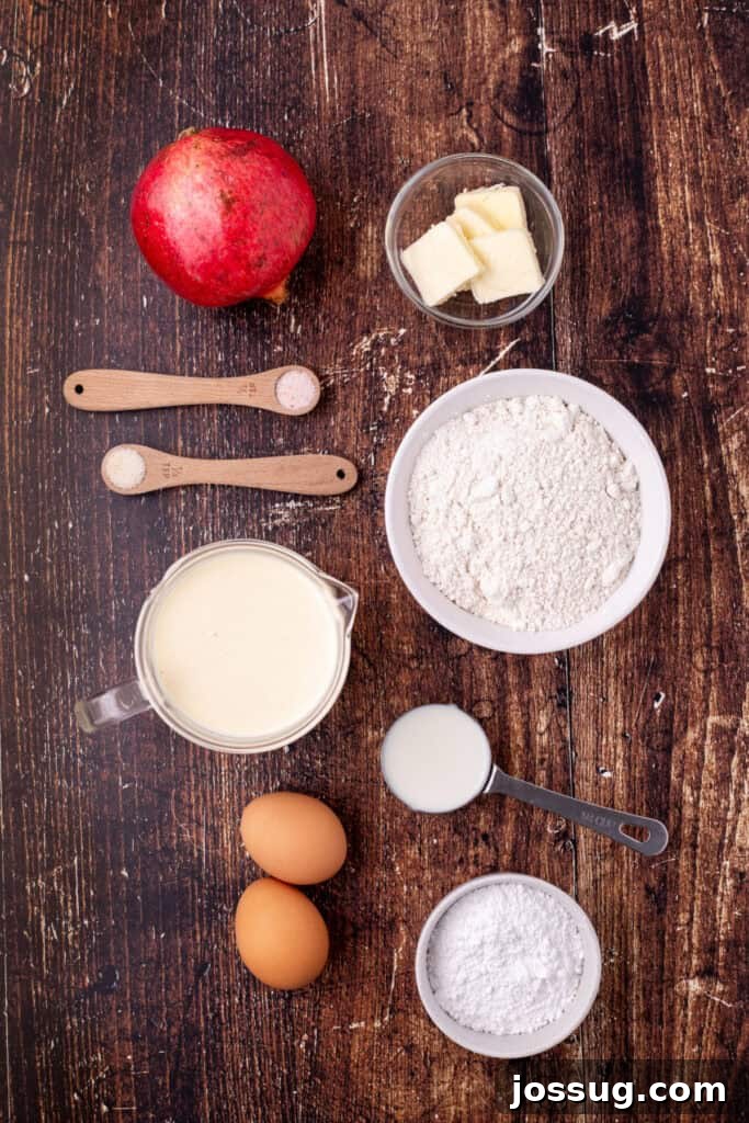 Overhead view of ingredients for eggnog crepes on a rustic wood surface including flour, butter, eggs, milk, eggnog, pomegranate, salt, and sugar, arranged for easy visibility.