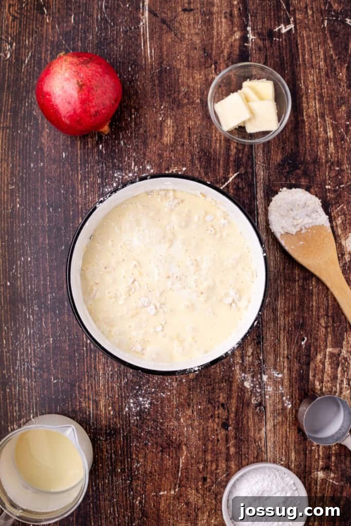 Mixing bowl with flour mixture and eggnog being combined to form crepe batter, surrounded by various baking ingredients on a wooden table, showing the liquid integration.
