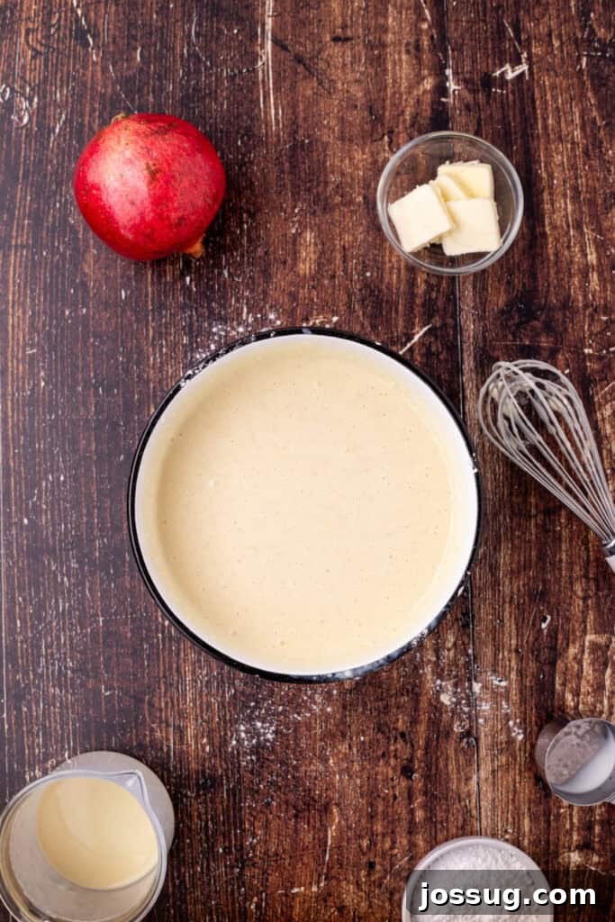 Smooth eggnog crepe batter in a bowl after whisking, with ingredients and utensils visible on a rustic wooden surface, indicating readiness for cooking.
