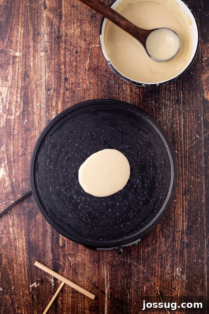 A small amount of eggnog crepe batter poured onto the center of the pan, ready to spread for cooking, showing the initial pour.