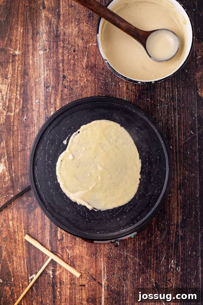 Eggnog crepe batter spread thinly across the cooking surface, forming a circular shape on the pan, demonstrating the swirl technique.