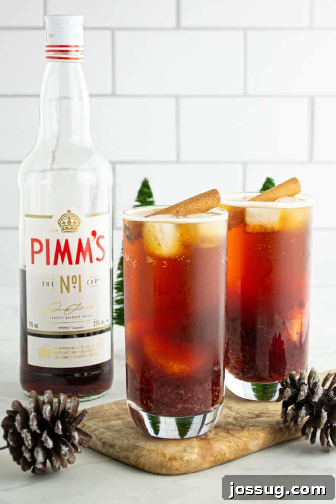 Crimson Pimms Delight 2 Two Cranberry Pimm’s Cocktails on a wooden board with Pimm’s No.1 bottle and ginger beer in the background, set in a festive holiday scene.