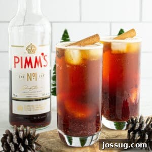 Crimson Pimms Delight 11 Two glasses of Cranberry Pimm’s Cocktail garnished with cinnamon sticks, surrounded by pinecones and festive décor.