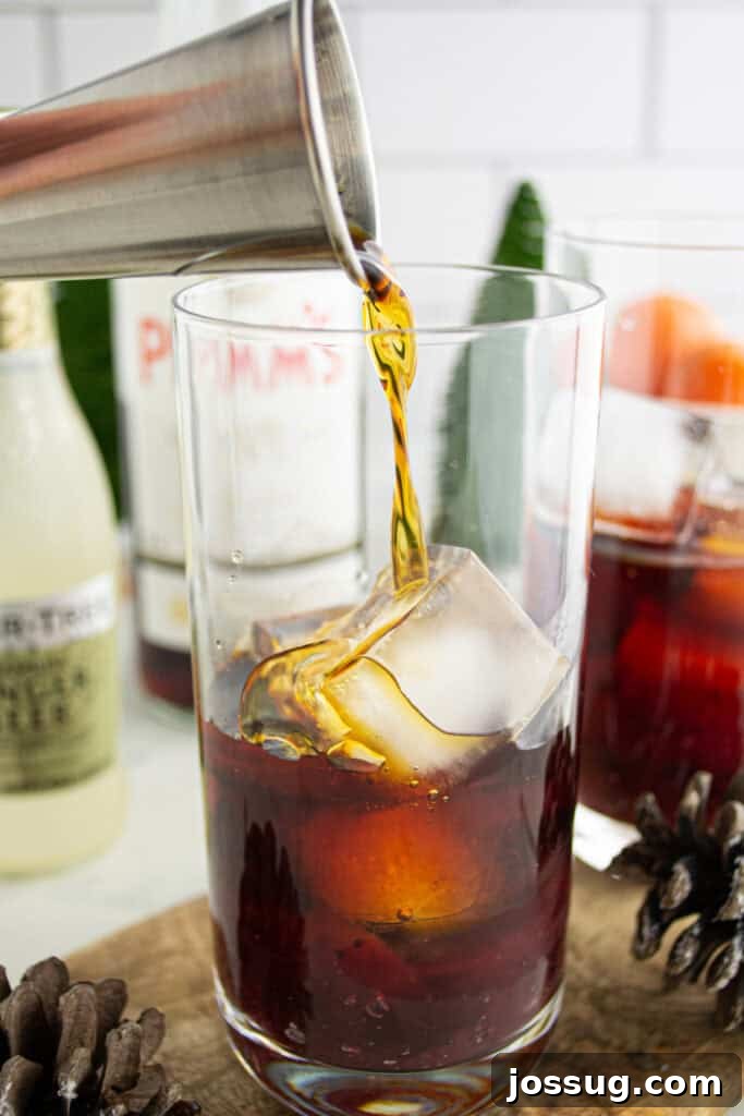 Crimson Pimms Delight 5 Pouring Pimm’s liqueur into a glass filled with ice and cranberry sauce to make a Cranberry Pimm’s Cocktail, highlighting the liquid being added.