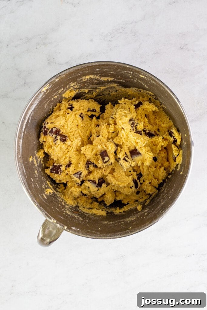 A mixing bowl filled with rich, thick cookie dough generously studded with large semi-sweet chocolate chunks, ready for scooping and baking.