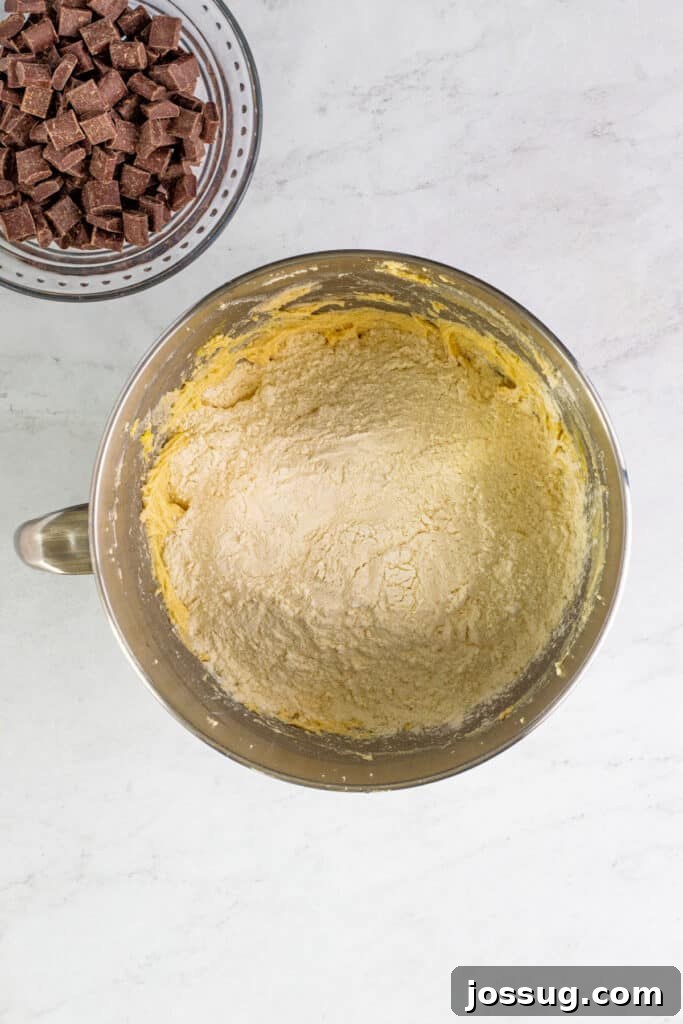Dry ingredients (flour mixture) gently layered on top of the wet mixture in a large mixing bowl, before being combined into cookie dough.