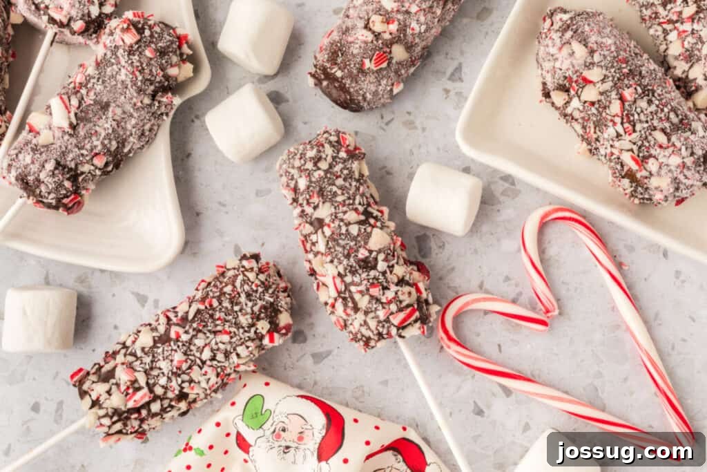 Peppermint Cloud Wands 13 Multiple finished peppermint coated marshmallow wands scattered artfully on plates and a light countertop, surrounded by loose marshmallows and decorative candy canes, highlighting their festive appeal.