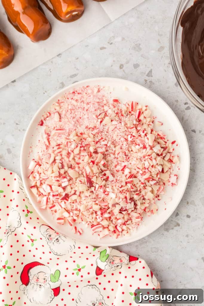 Peppermint Cloud Wands 8 A shallow plate generously filled with crushed peppermint candy, showing various sizes of vibrant red and white pieces, perfectly prepared for coating the freshly chocolate-dipped marshmallow wands.