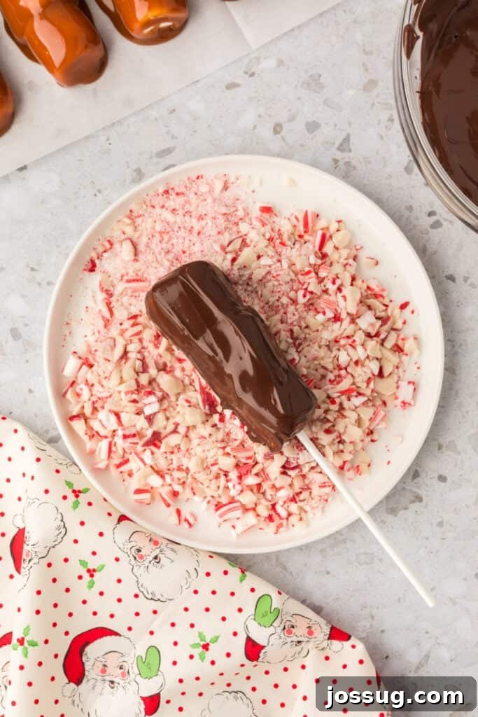 Peppermint Cloud Wands 9 A caramel-coated marshmallow wand being carefully dipped into a pool of melted dark chocolate, then gently placed onto a plate of crushed peppermint, ready for its final festive coating.