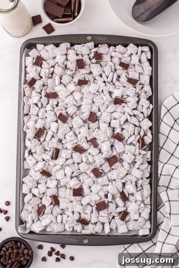 Close view of Thin Mint Muddy Buddies spread on a baking sheet with extra Andes mint pieces on top.