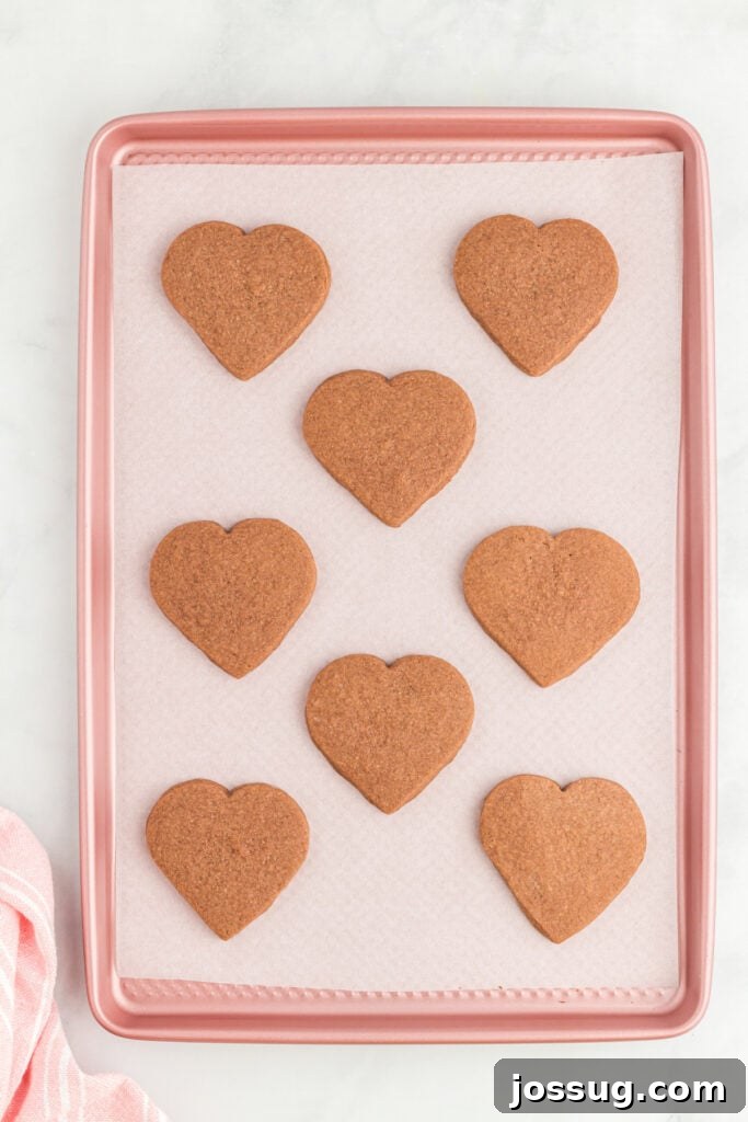 Baked heart-shaped chocolate cookies cooling on a baking sheet.