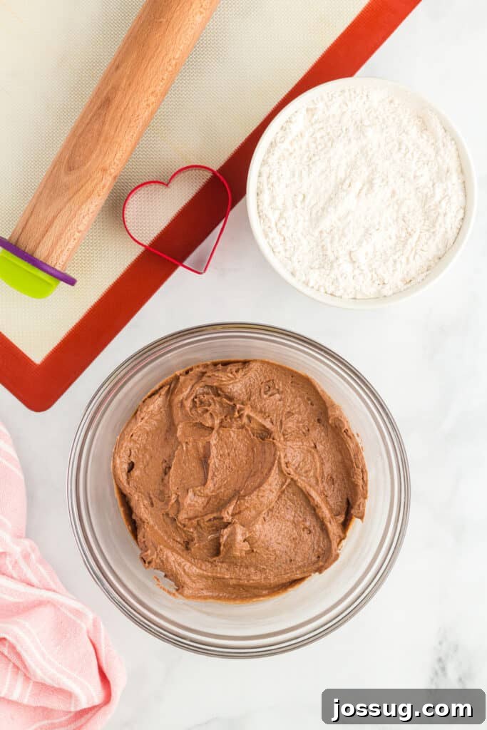 Chocolate cookie dough in a bowl with rolling pin and heart cookie cutter.