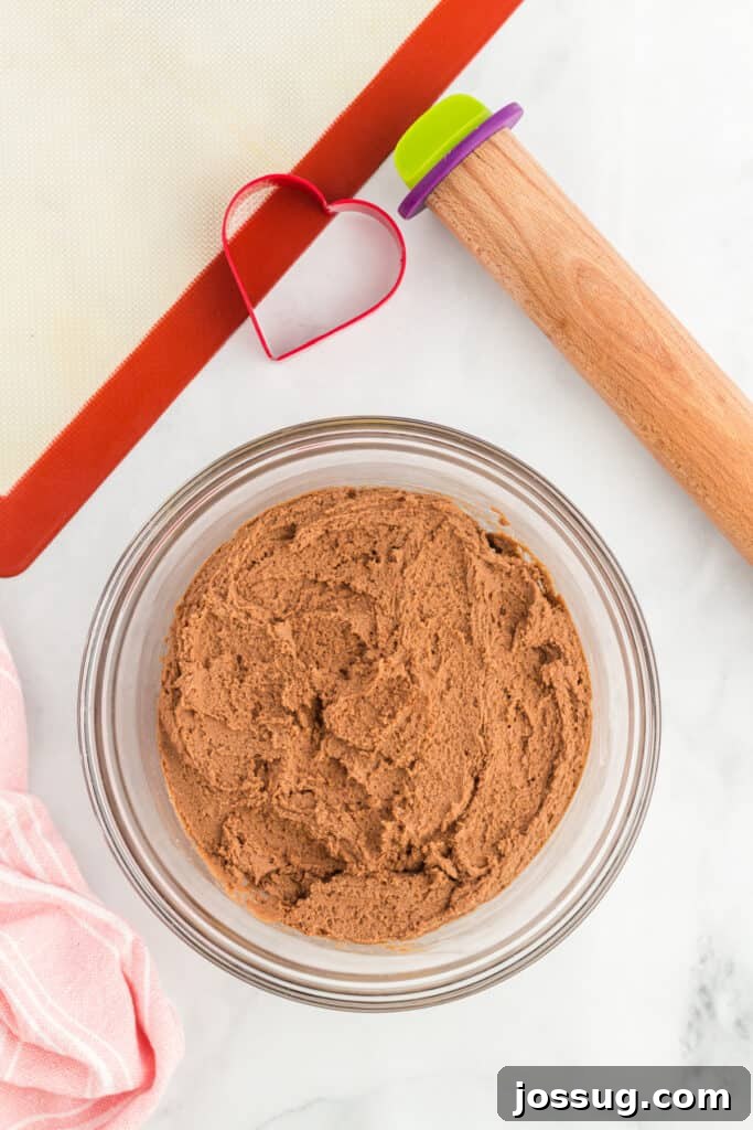 Thick chocolate cookie dough with rolling pin and heart cookie cutter.