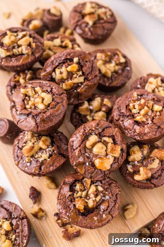 Pile of turtle brownie bites on a wooden board, topped with walnuts, caramel drizzle, and sea salt.
