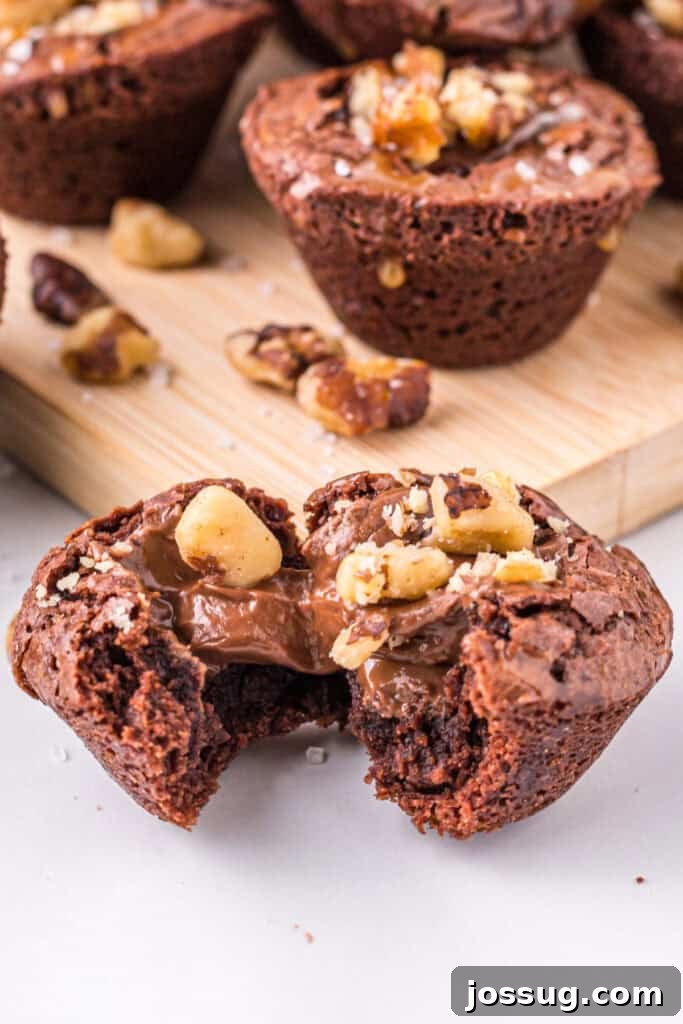 Close up of a turtle brownie bite broken open to show melted chocolate and chopped walnuts in the center, with more brownie bites behind it.