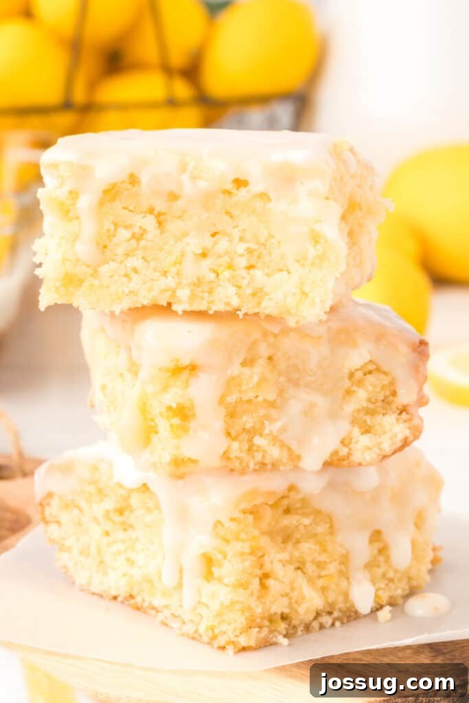 Closeup of three lemon brownies stacked on top of each other, generously coated with a glistening lemon glaze
