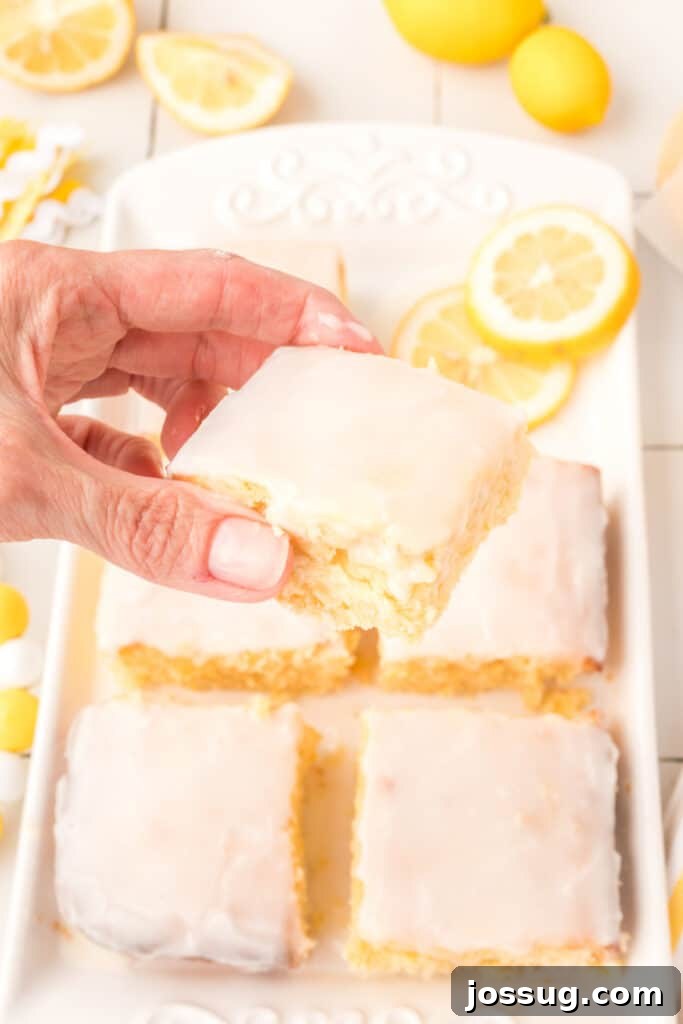 Hand holding a square slice of lemon brownie with a perfect glaze, ready to eat