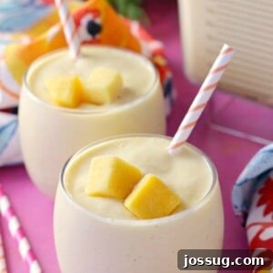 A vibrant yellow Sunshine Smoothie with Banana and Mango in a glass, garnished with fresh fruit, on a bright background.