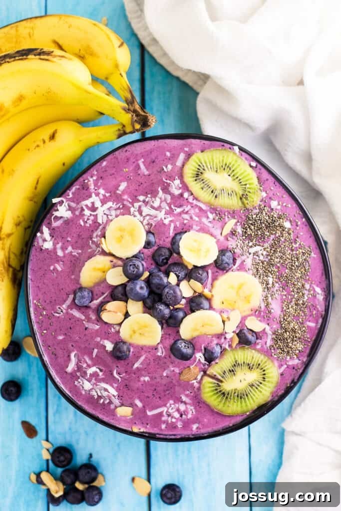 Looking down onto a vibrant blueberry banana smoothie bowl, garnished with fresh fruit and seeds.