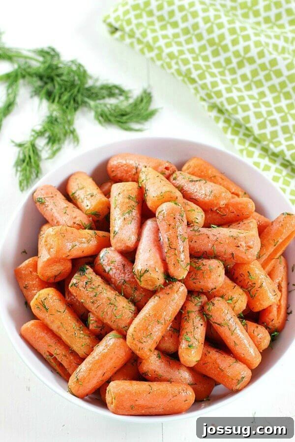 Close-up of Dill Butter Carrots in a white bowl, garnished generously with fresh dill sprigs, highlighting the herb's fresh appeal.