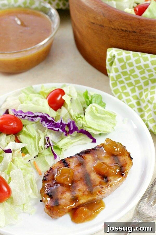 Tangy Peach Glazed Pork Chops 5 A delicious Dijon-Peach Pork Chop served alongside a fresh green salad on a white plate.