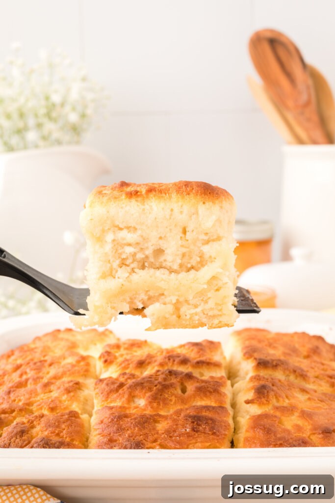 A freshly baked butter dip biscuit being lifted from a baking dish with a spatula, ready to be topped with jelly.