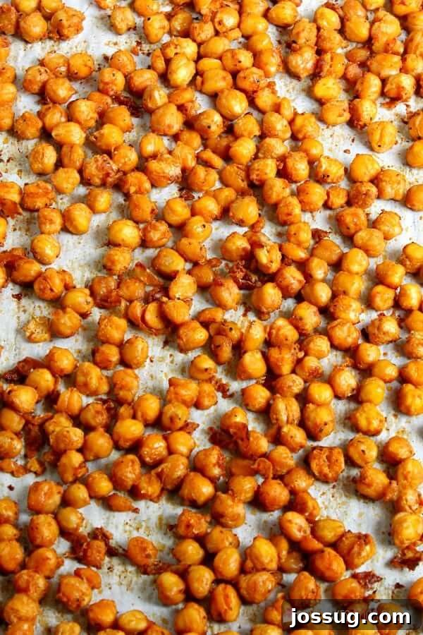 Spicy roasted chickpeas spread evenly on a parchment-lined baking sheet, showing their crispy texture.