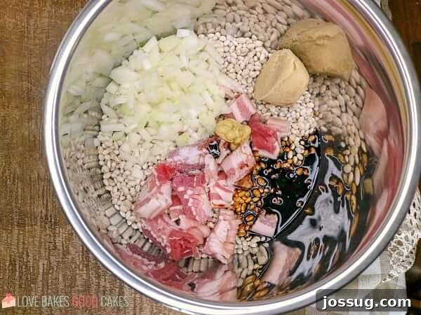 Close-up of dried navy beans and other raw ingredients for baked beans in a mixing bowl, prior to cooking.