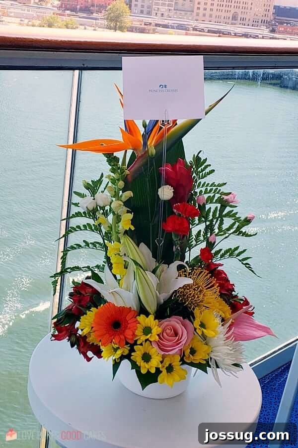 A tranquil scene on a cruise ship balcony: a beautiful flower arrangement and a card rest on a small table, with a bustling harbor view in the background, highlighting the comfort of a private outdoor space.