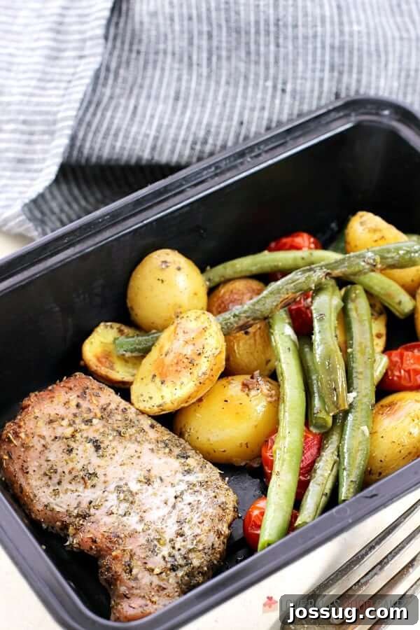 A storage container holding a serving of Italian Pork Chop Sheet Pan Dinner, complete with a fork, emphasizing its convenience for meal prepping.