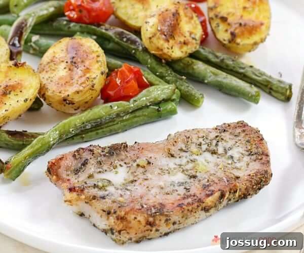 Close-up detail of a single serving of Italian Pork Chop Sheet Pan Dinner on a white plate, highlighting the perfectly roasted ingredients.