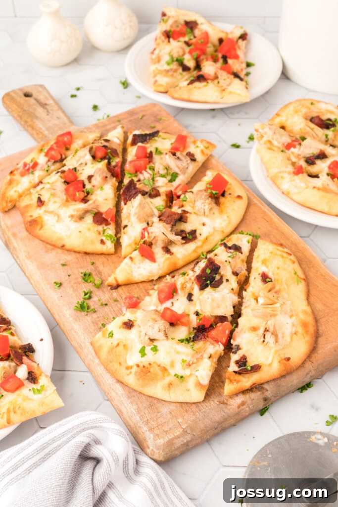 Close-up of a Chicken Bacon Ranch flatbread pizza on a wooden cutting board, showcasing its vibrant toppings.