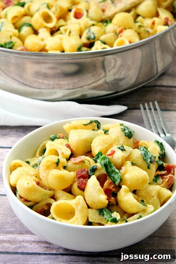 Effortless Creamy Bacon Spinach One-Pot Pasta 6 One-Pot Creamy Bacon Spinach Pasta served in a white bowl with a fork, alongside the skillet it was cooked in.