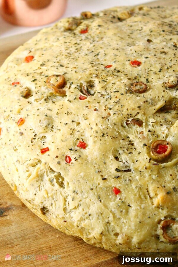 Crusty No-Knead Skillet Olive Bread on a wooden cutting board, showcasing its rustic texture.