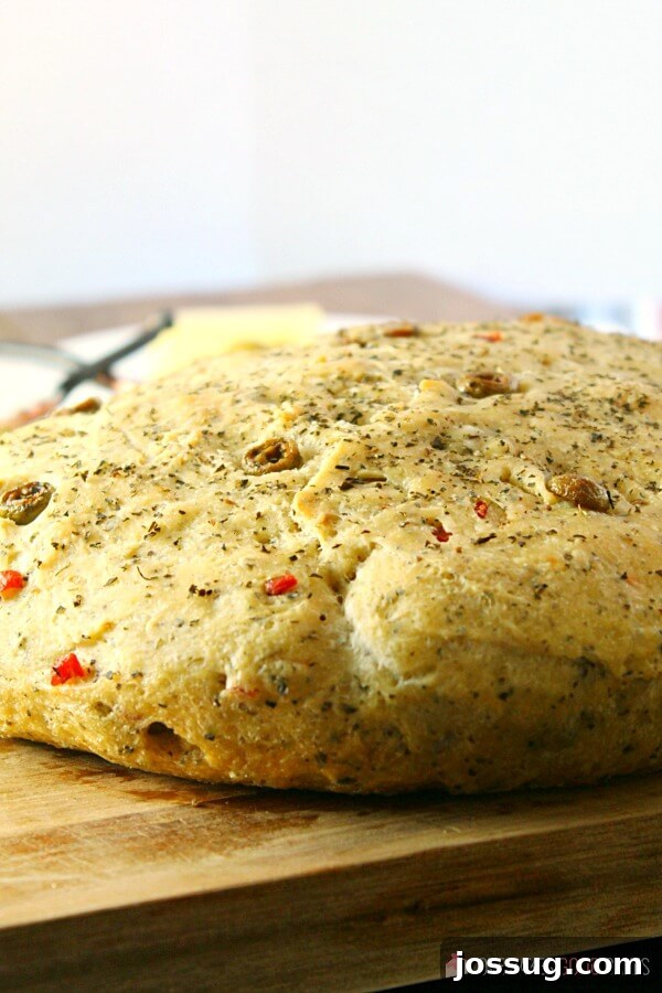 A freshly baked loaf of No-Knead Skillet Olive Bread resting on a cutting board, ready to be sliced.