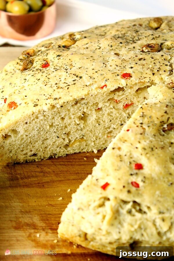 A beautiful loaf of No-Knead Skillet Olive Bread with a slice cut out, ready to serve.