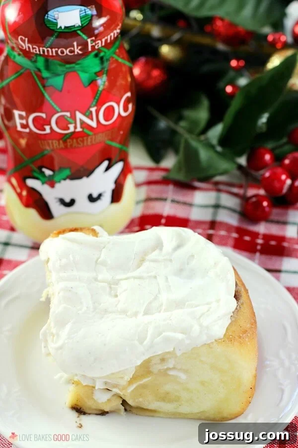 Festive Eggnog Cinnamon Rolls 5 A close-up of a single Eggnog Cinnamon Roll on a white plate, showcasing its soft, moist texture and the thick, creamy layer of eggnog frosting, with a glass of eggnog in the background.