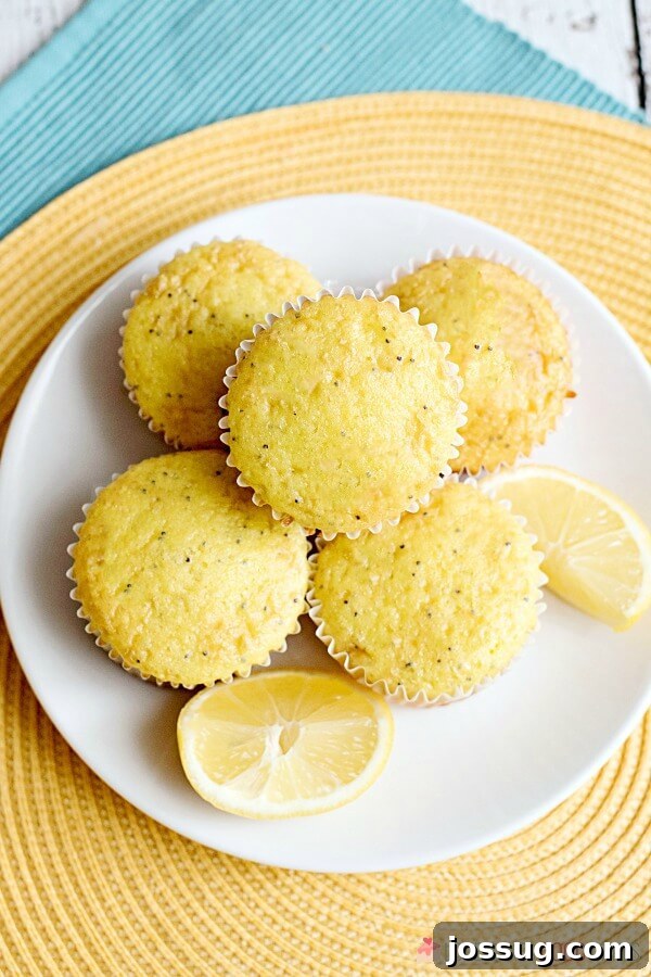 A generous pile of freshly baked Lemon Poppy Seed Muffins artfully arranged on a white plate, garnished with vibrant fresh lemon wedges, ready for serving.