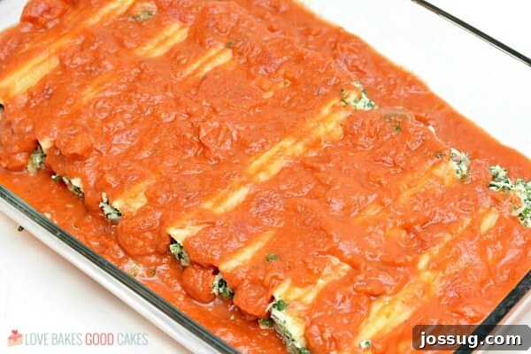 Spinach Ricotta Manicotti covered in red marinara sauce in a baking dish, bubbling hot.