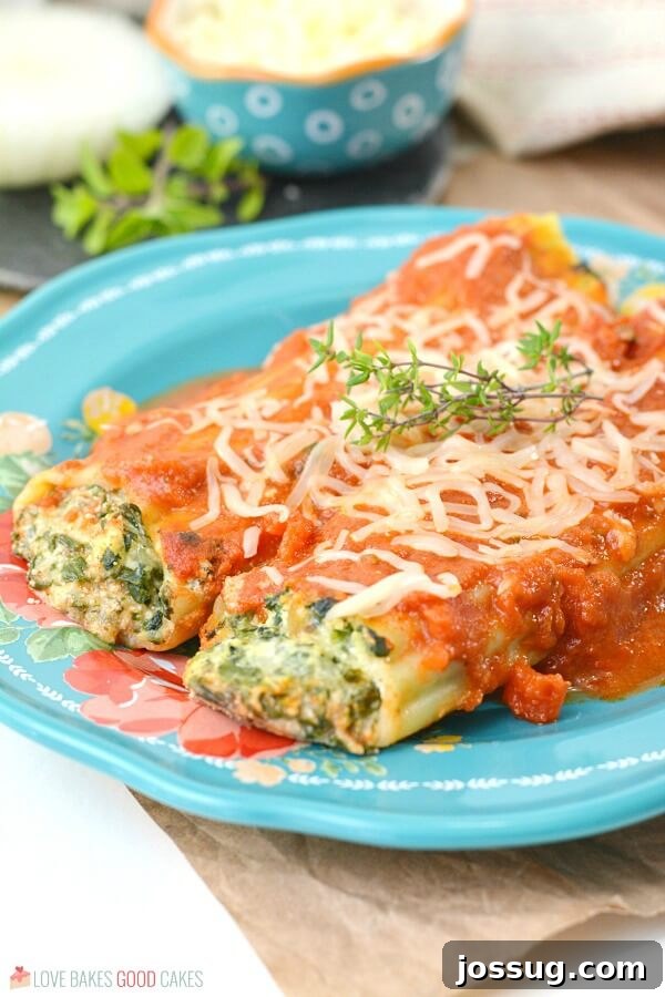 Close up of spinach ricotta manicotti on a blue plate, showing the creamy filling and sauce.