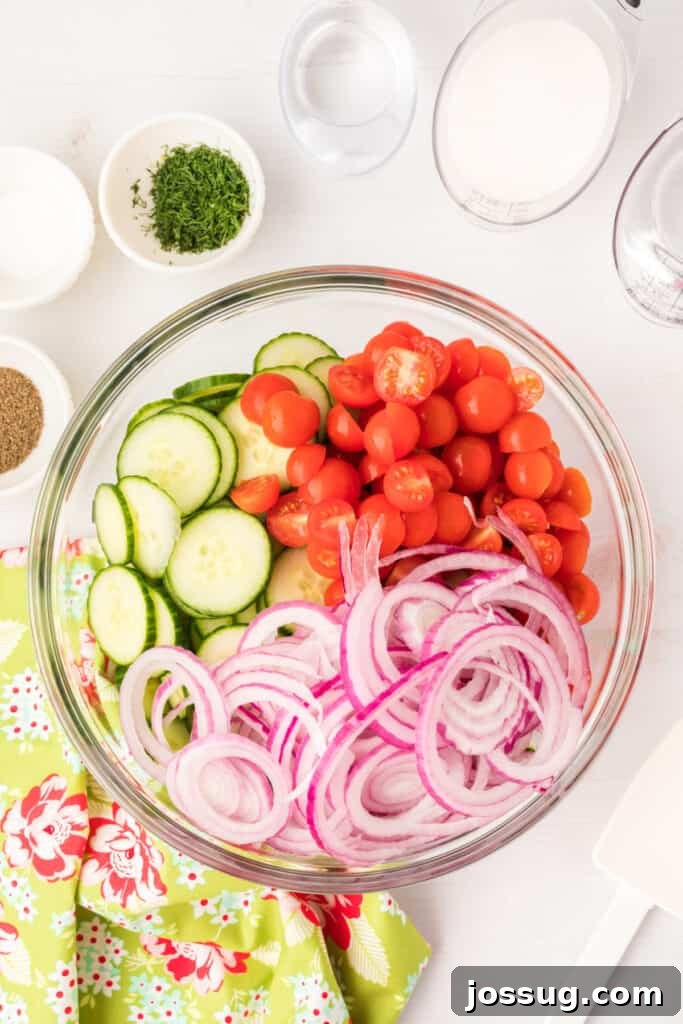 Vibrant Cucumber Tomato Medley 4 A selection of fresh, vibrantly colored vegetables for the salad, including thinly sliced cucumbers, halved cherry tomatoes, and finely sliced red onions, all neatly arranged in a glass bowl with seasonings nearby.