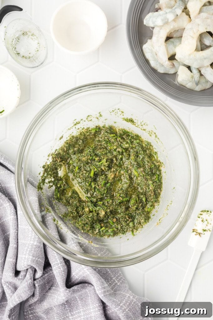 The grilled shrimp marinade, a vibrant yellow and green mixture, fully mixed in a clear bowl and ready for the shrimp.