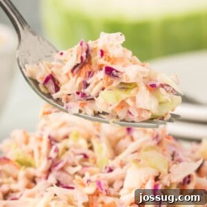 Square close-up of a forkful of creamy coleslaw lifted above a full bowl of salad.