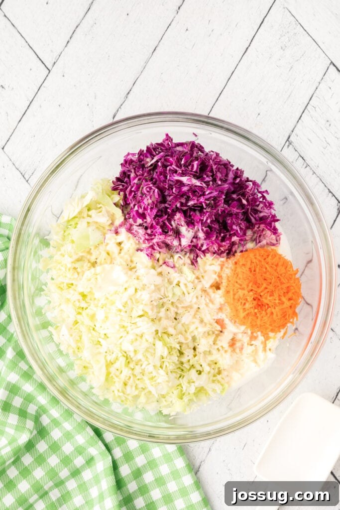 Large glass bowl filled with shredded green cabbage, red cabbage, and carrots before mixing.