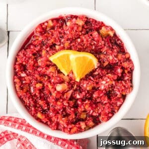 Overhead square image of cranberry relish in a white bowl topped with orange slices, showcasing its vibrant red color and fresh texture.
