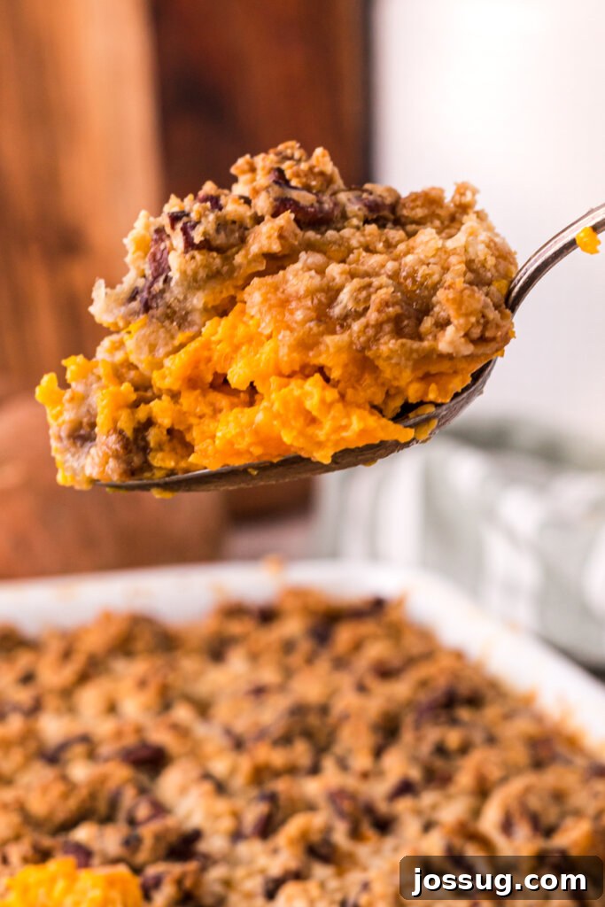 A close-up view of a spoonful of sweet potato casserole, showing its creamy texture and the crunchy pecan topping.