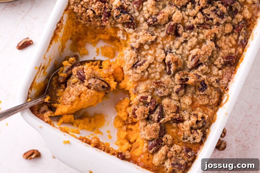 A serving spoon lifting a portion of sweet potato casserole, showcasing the layers of creamy sweet potato and crunchy pecan topping.