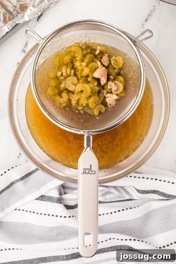 Strainer with cooked celery and bits of turkey over a glass bowl of broth for gravy preparation.